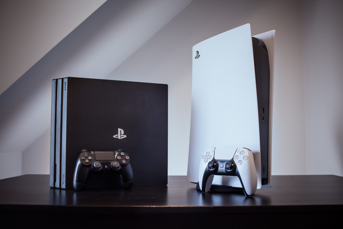 Ps4 in black and Ps5 in white plced on the table with their respective controllers representing the comparison between PlayStation 5 and PlayStation 4 Pro gaming consoles.