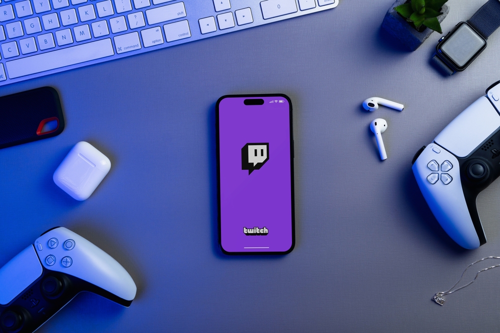 Twitch app on the smartphone iPhone 14 Pro screen with PS5 video game controllers. Top view.