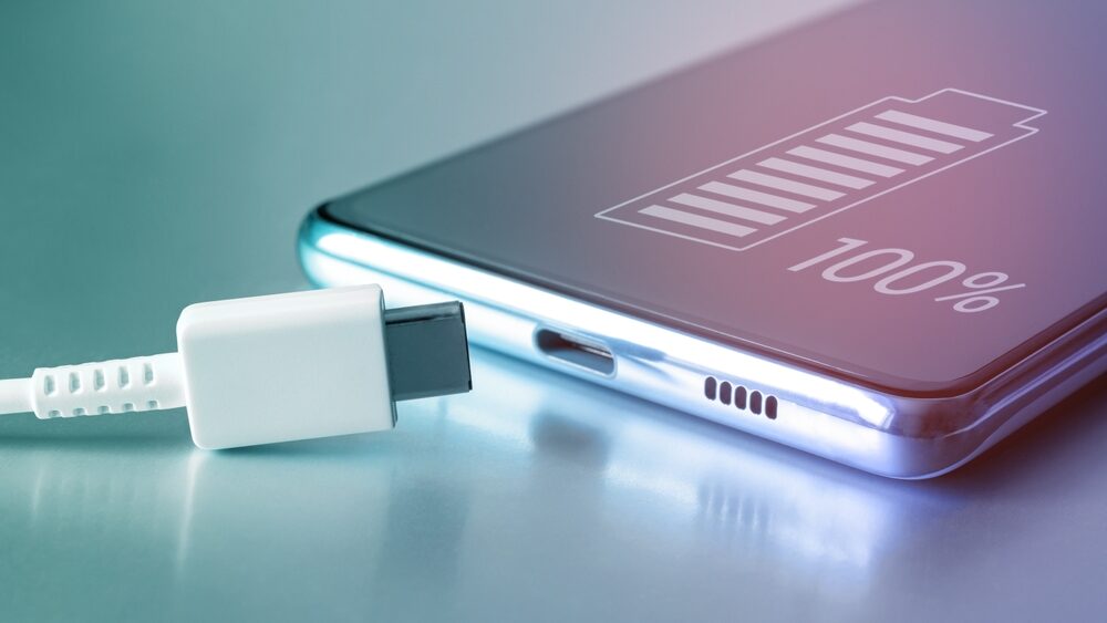 Close up of charger pin with smartphone and its screen shows 100% battery representing improved battery life of new smartphones