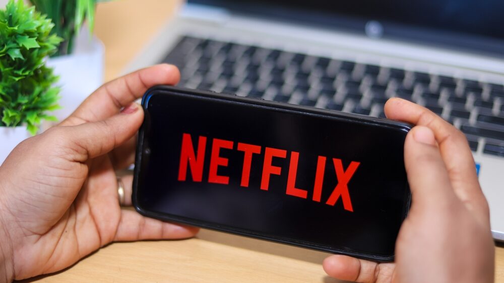 Man holding a smartphone showing the Netflix logo on the mobile phone screen.